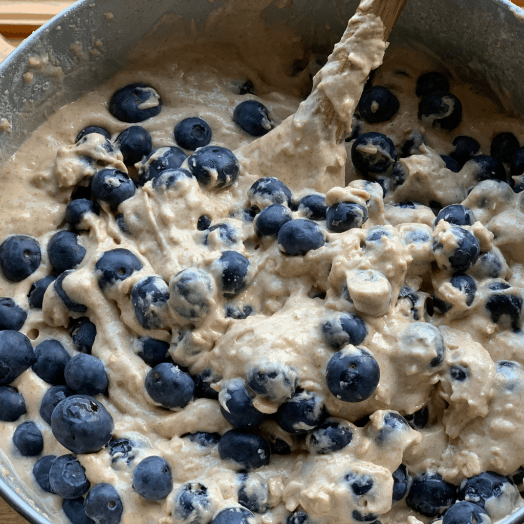 Fresh blueberries in muffin mix batter that is made is rolled oats, cinnamon and other healthy ingredient swaps.