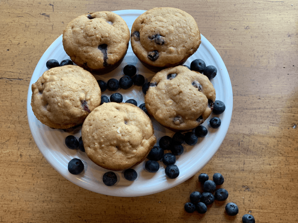 Oatmeal blueberry muffin recipe with five muffins on a plate surrounded by fresh blueberries.