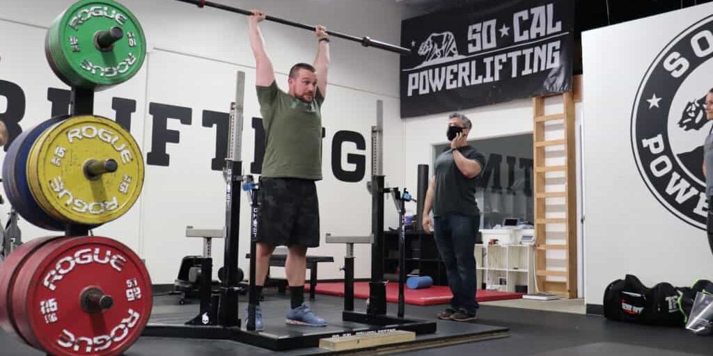 Powerlifting athlete with an unloaded barbell over his head in an active recovery session to promote increased performance.