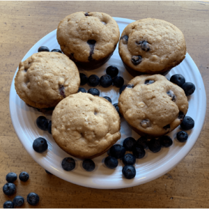 A plate with 5 oatmeal blueberry muffins and fresh, extra large blueberries surrounding the muffins.