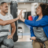 Man and woman on exercise equipment celebrating that fitness is for everyone by giving a high-five.